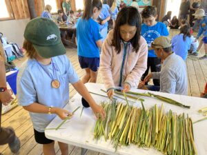 Young campers gathering cut pieces of tule reeds laid on a table.