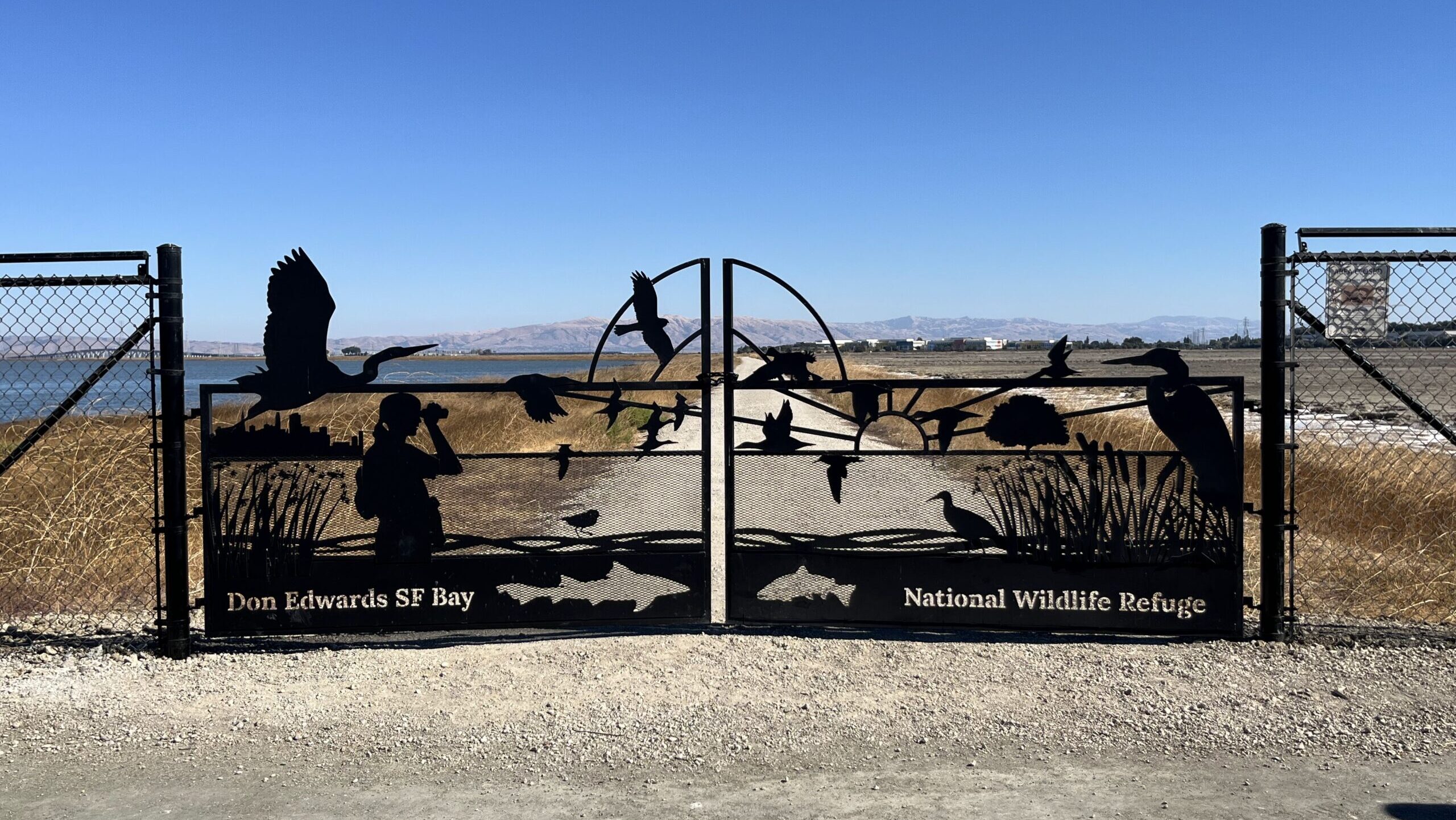 Decorative gate at the Flyway Trail featuring silhouettes of birds, fish, landscape, and a bidrwatcher.